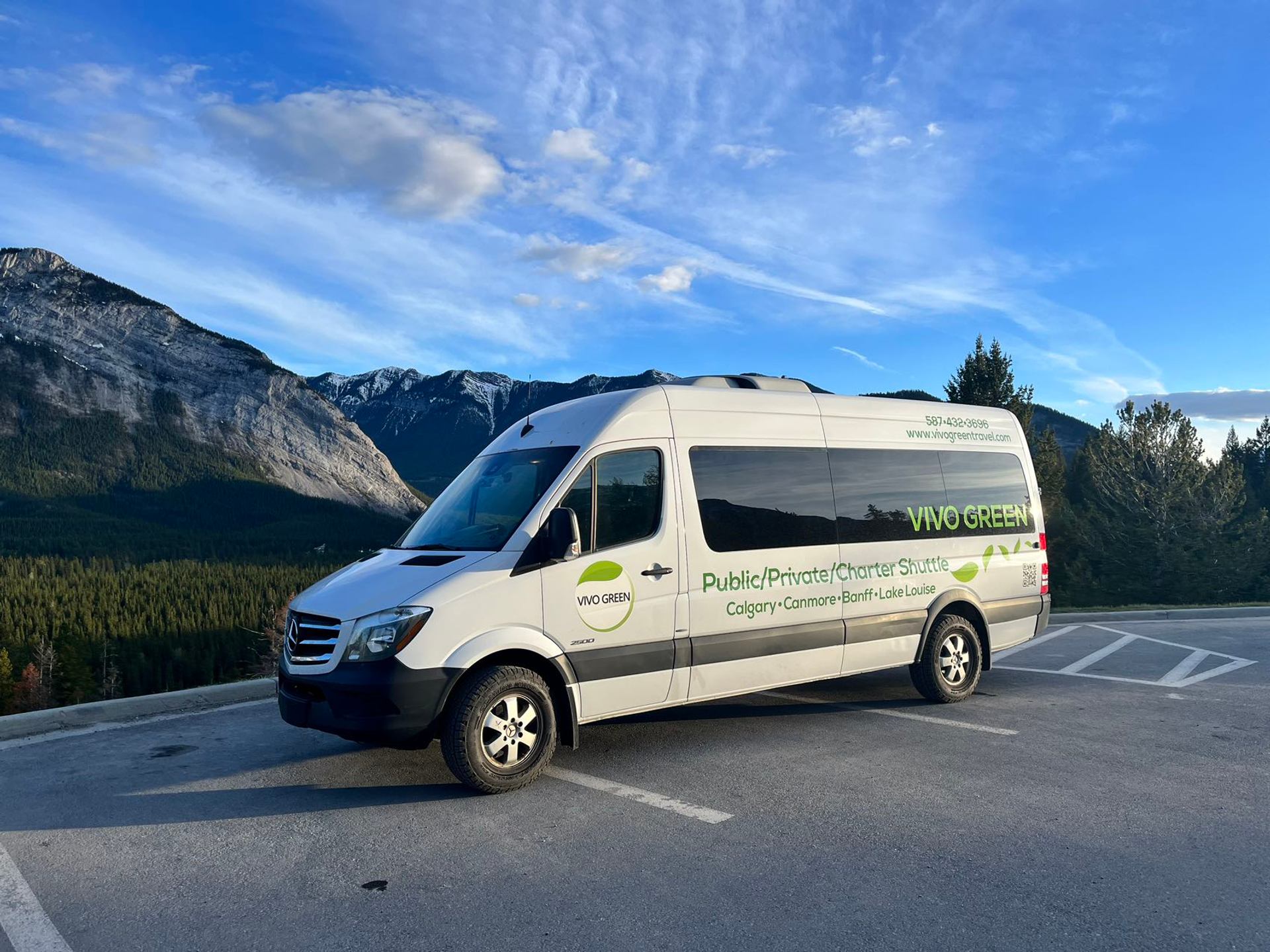 Vivo Green shuttle van parked at a mountain viewpoint under a blue sky.