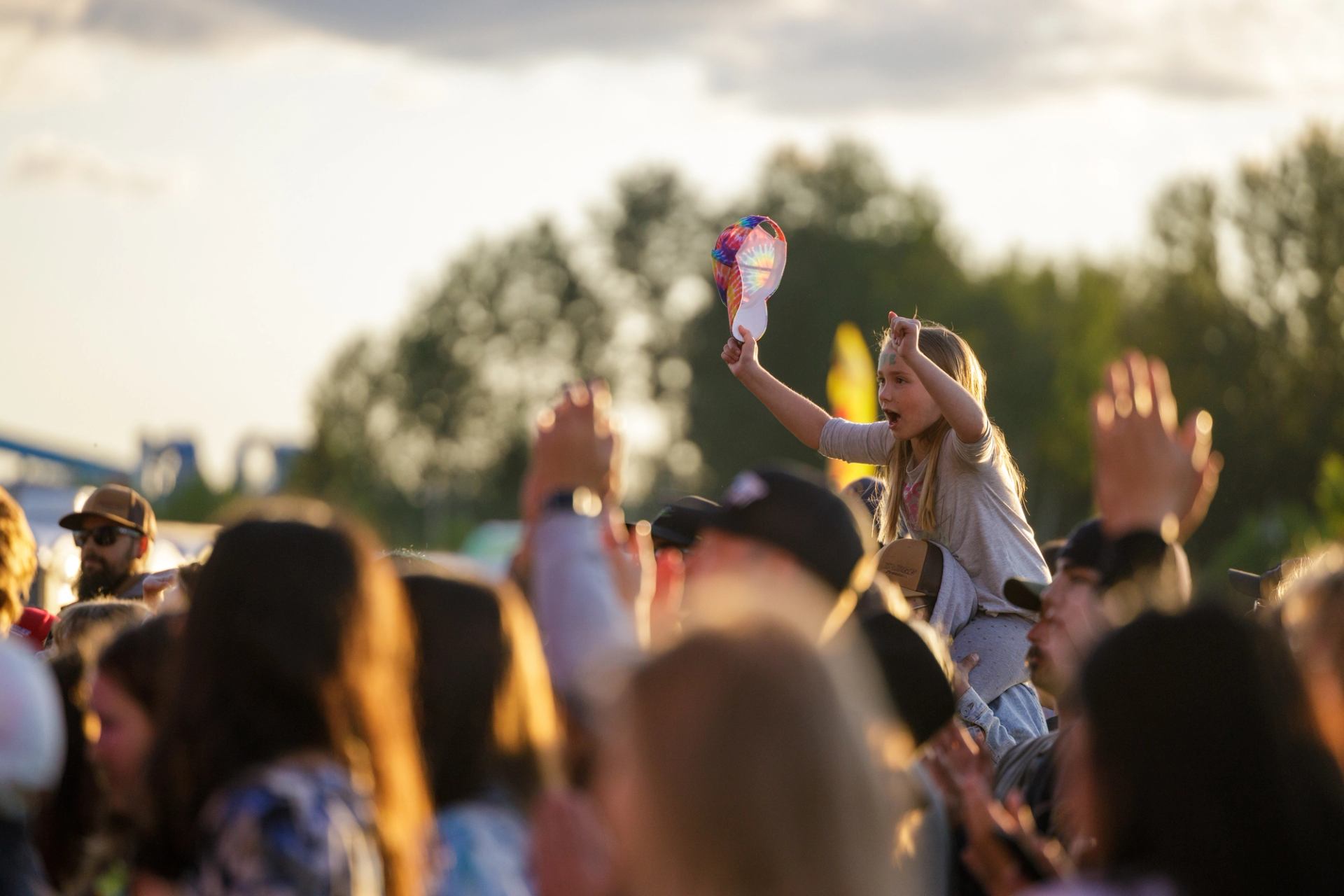 Festival crowd at sunset with someone raised above the crowd waving colorful gear.