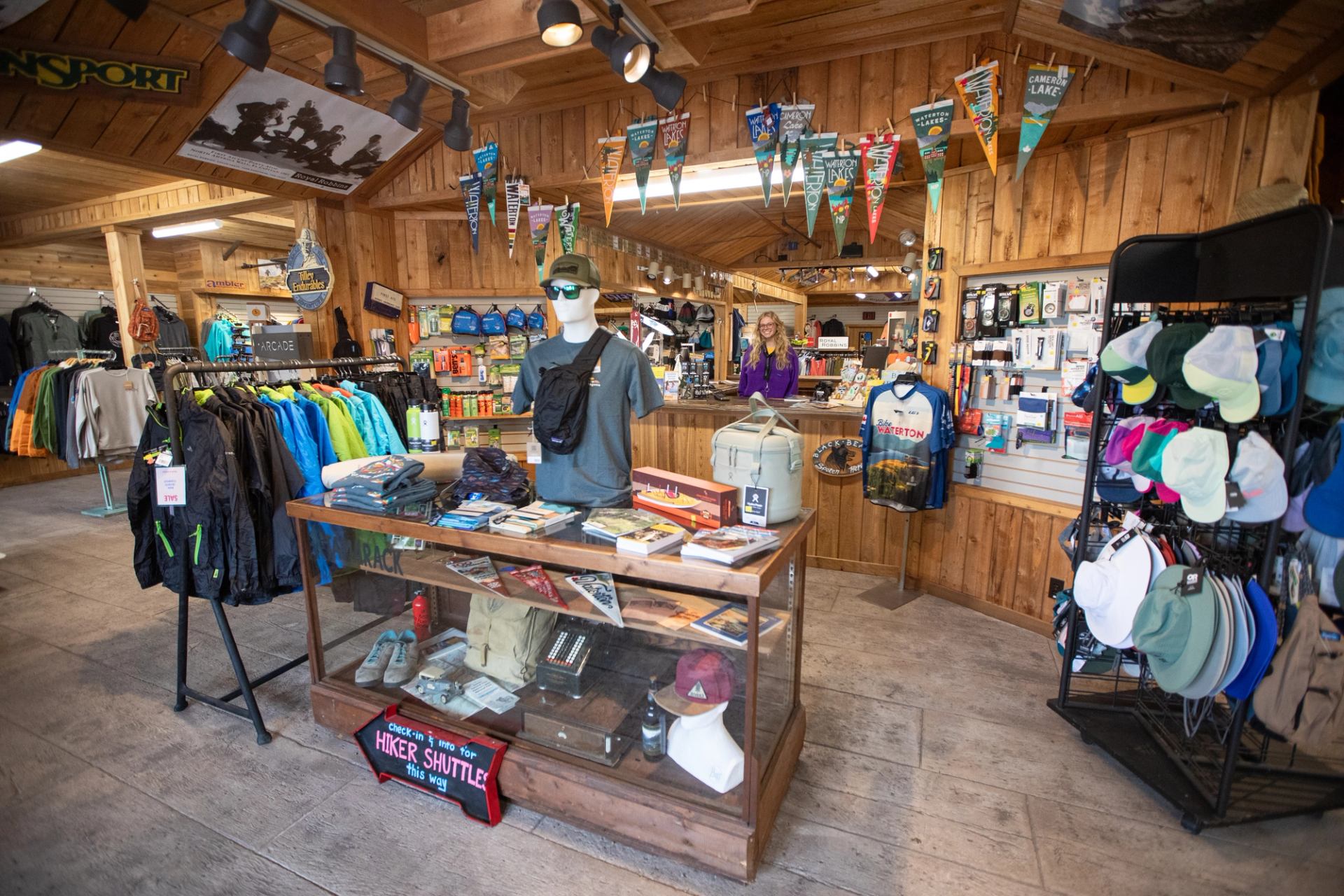 Outdoor gear shop interior with clothing racks, hats, souvenirs and staff behind wooden counter.