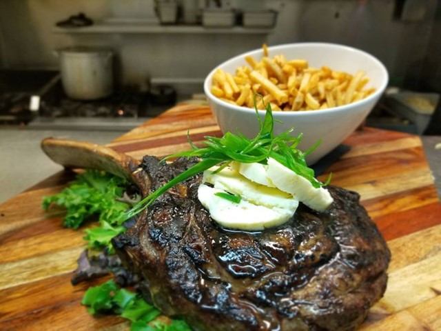 Steak with herb garnish and fries on a cutting board in a pro kitchen setting.