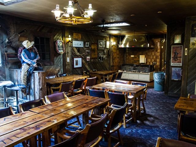 Rustic dining room with wooden tables, leather chairs, and cowboy-themed decor.