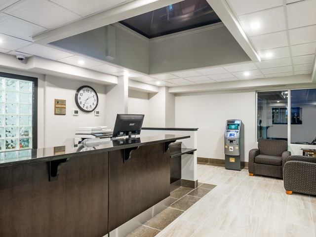 Hotel reception desk with computer, wall clock, ATM machine and two patterned armchairs.