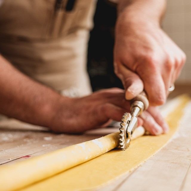 Close-up of hands using a pasta cutter on a long sheet of yellow dough on a wooden surface