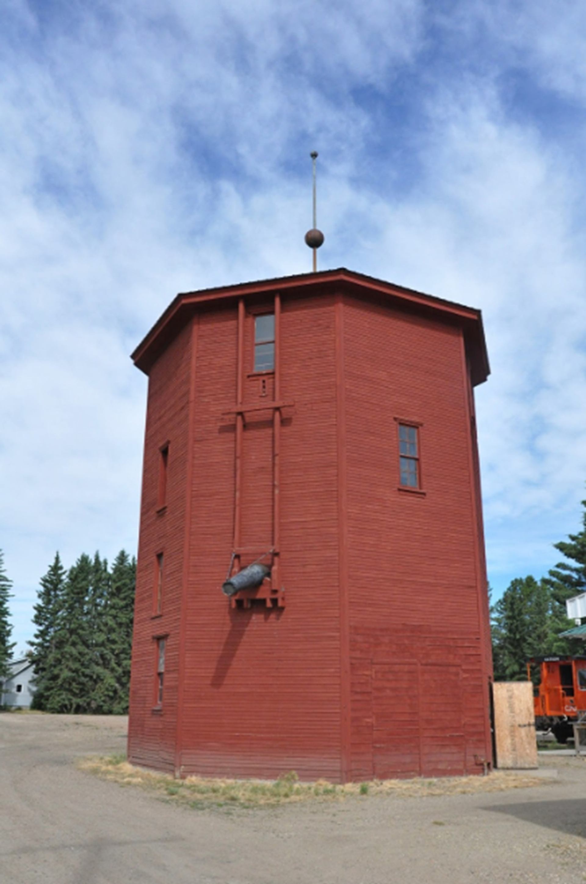Red wooden tower with exterior hoisting equipment beneath a blue, cloud-filled sky.
