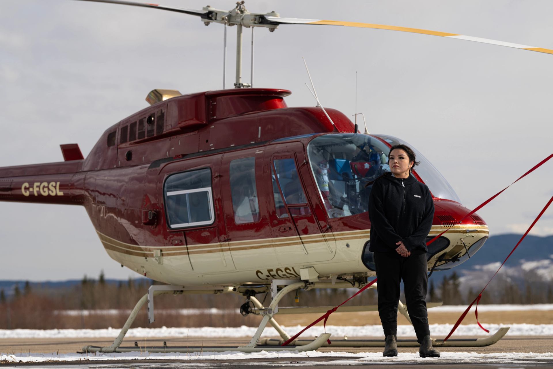 Red and white helicopter on snowy ground with person standing in front.