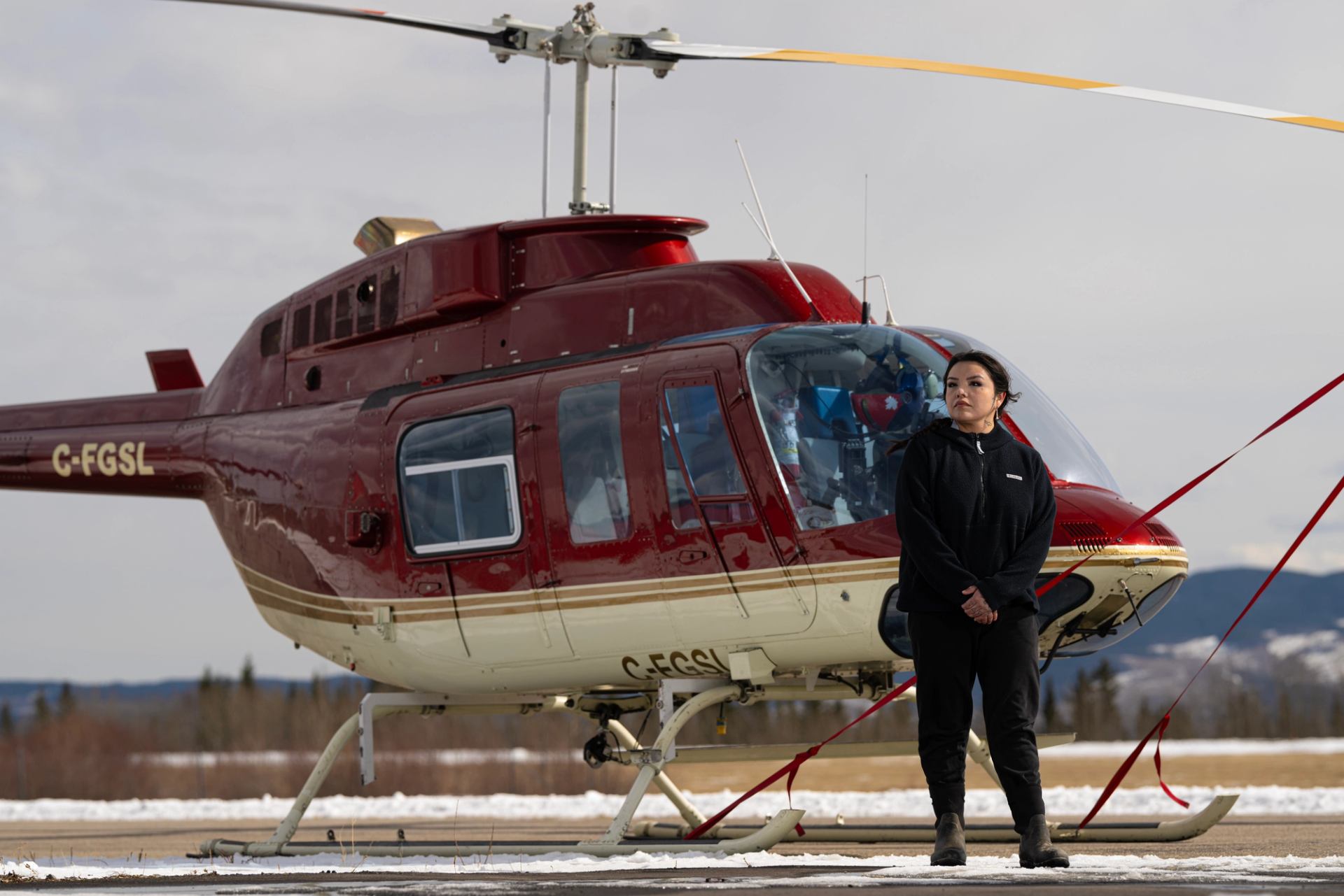 Red and white helicopter on snowy ground with person standing in front.