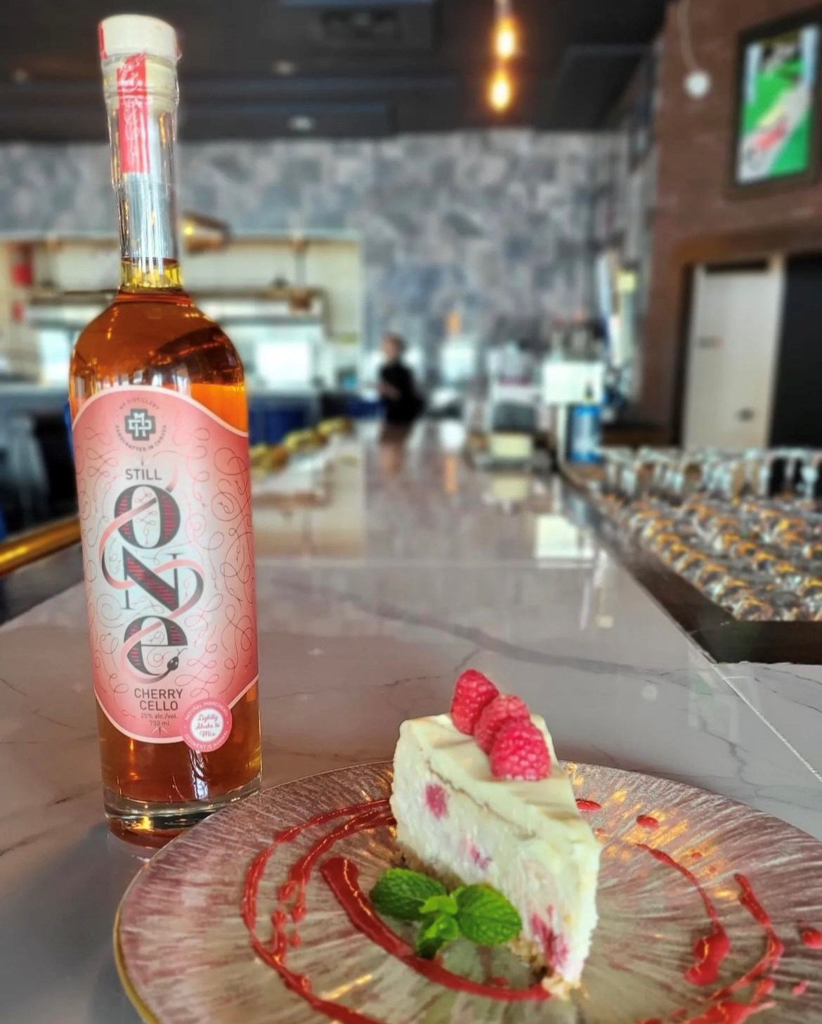 Wine bottle and slice of cheesecake with raspberries and mint on a table in a restaurant.