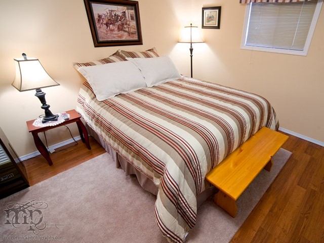 Cozy bedroom with striped bedding, wooden bench, and warm lighting.
