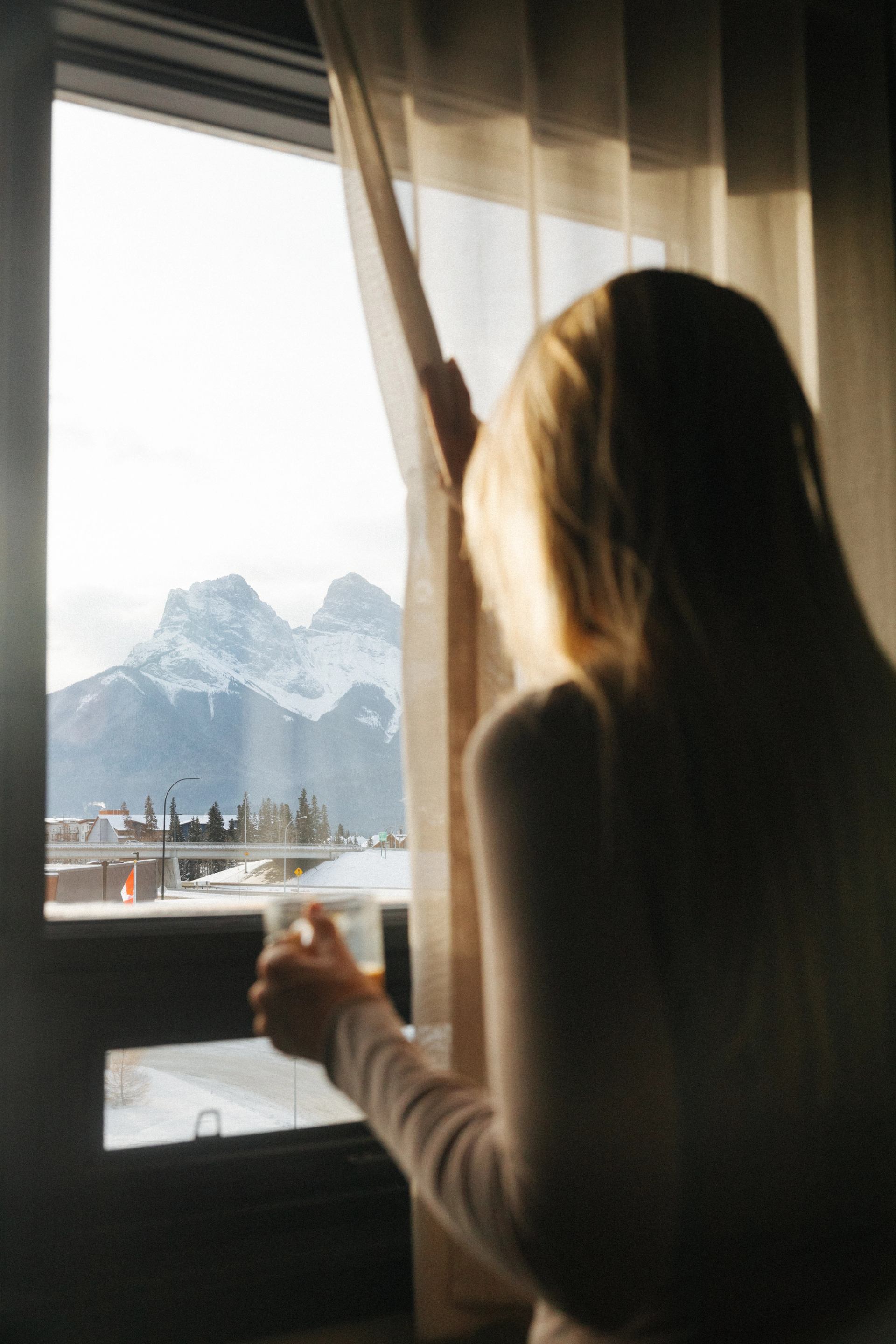 Person looking out hotel window at snow-covered mountains in Canmore.