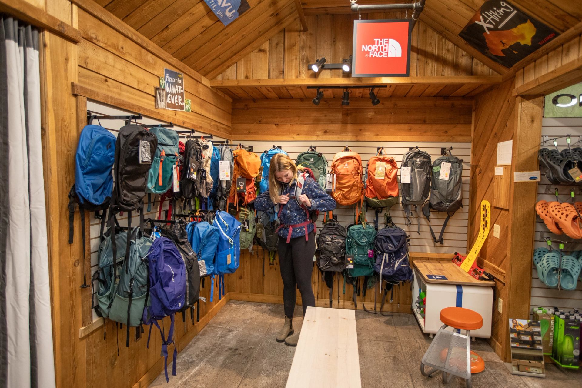 Outdoor gear shop interior with person trying on backpack among colourful packs.