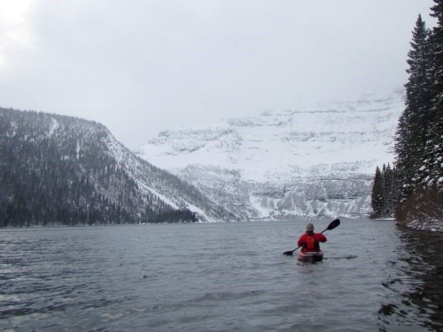 Person kayaking on a lake with snowy mountains in the background.