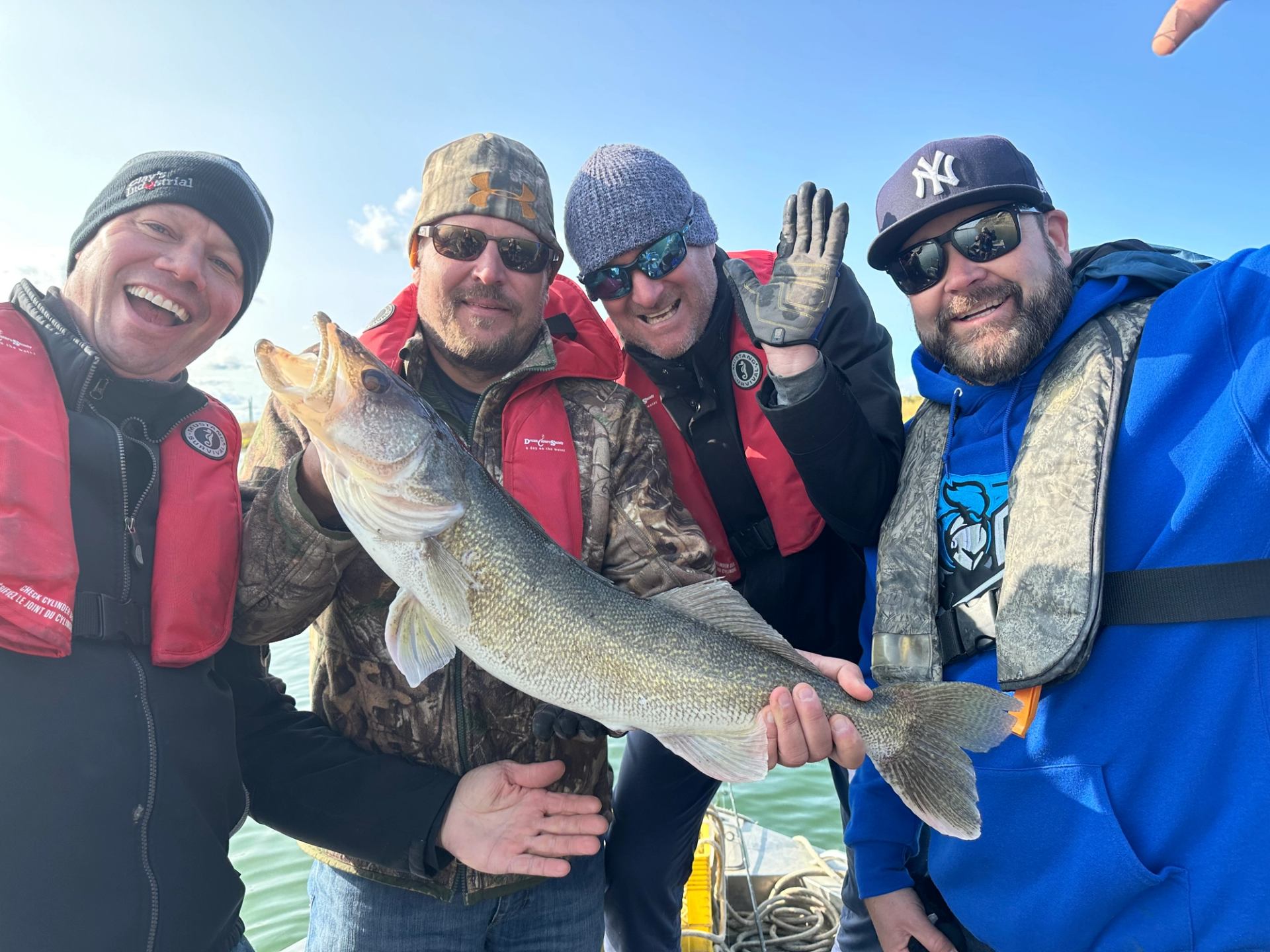 Four anglers in winter jackets hold large fish during ice-fishing adventure.