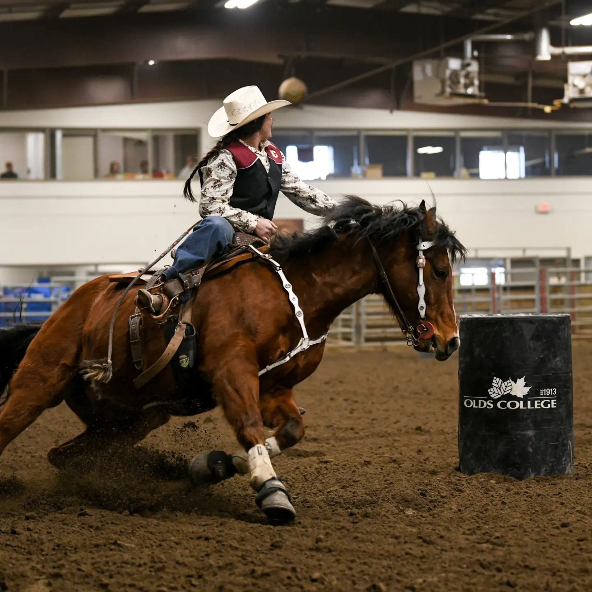 Rider on horseback making a sharp turn around a barrel in an indoor rodeo arena.