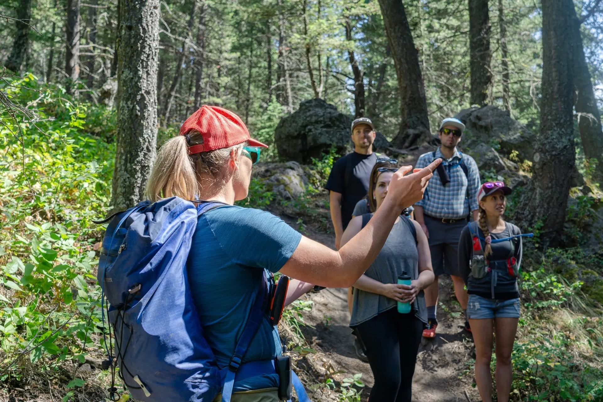 Hikers listen to a guide during a nature walk in a forest with trees and rocks.