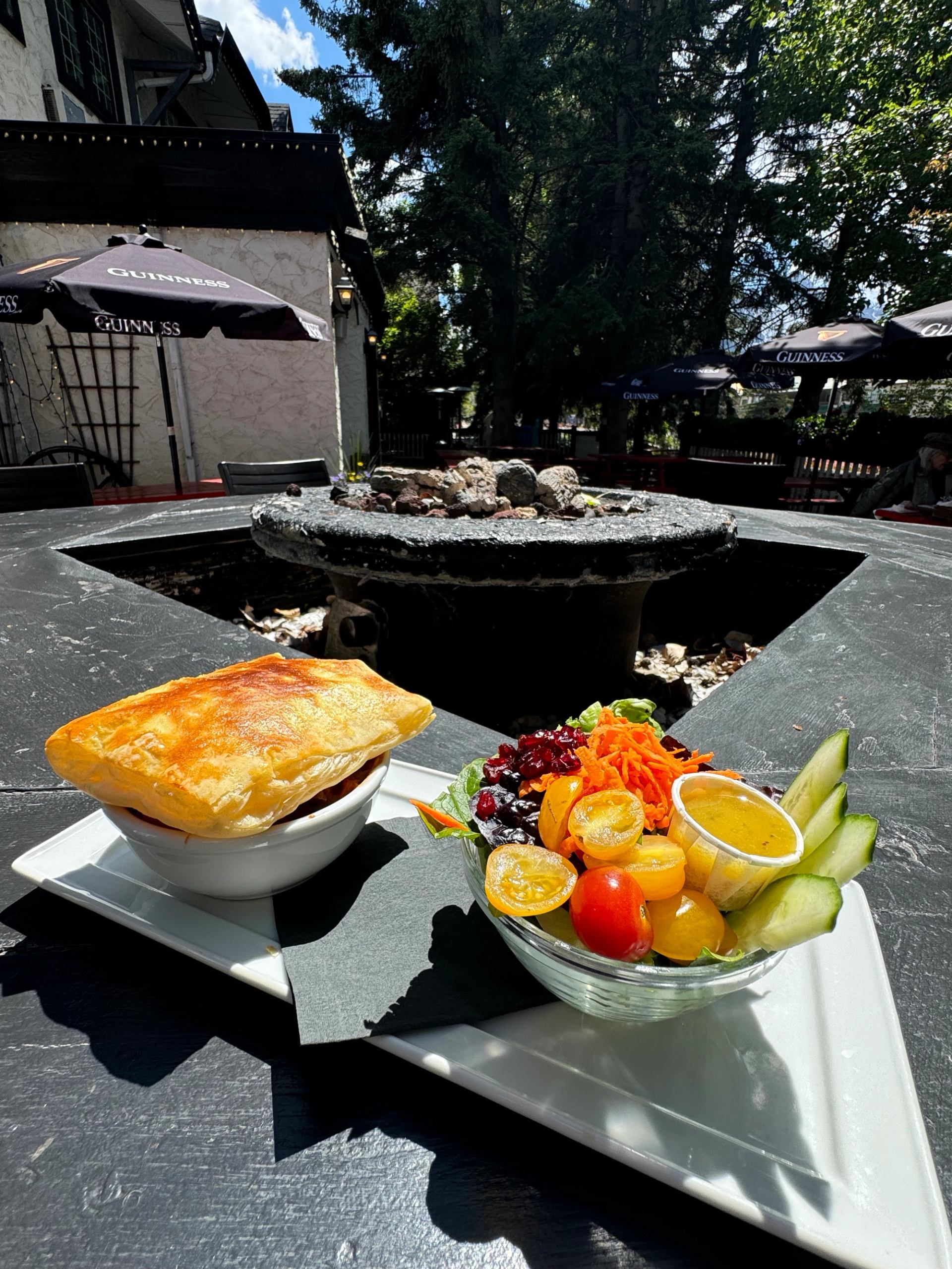 Outdoor table with pot pie and fresh veggie sides in elegant setting.