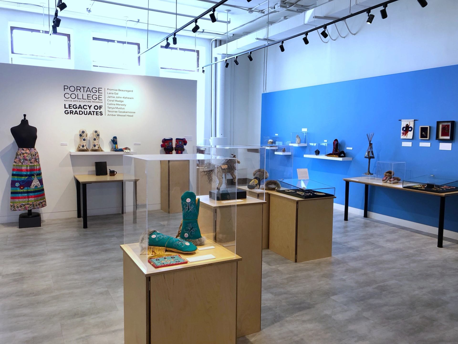 Art gallery interior with display cases, mannequins, and framed artwork on tables and walls.