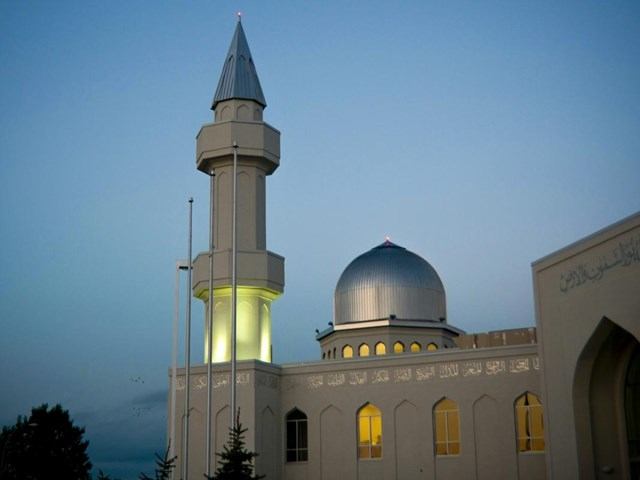 Exterior of Baitun Nur Mosque in Calgary with illuminated minaret and dome at dusk.