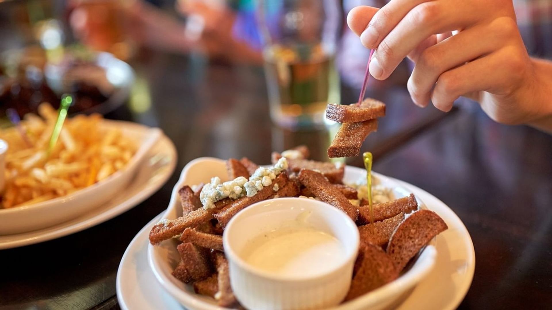 Plate of fried bread sticks with dip as hand lifts a piece.