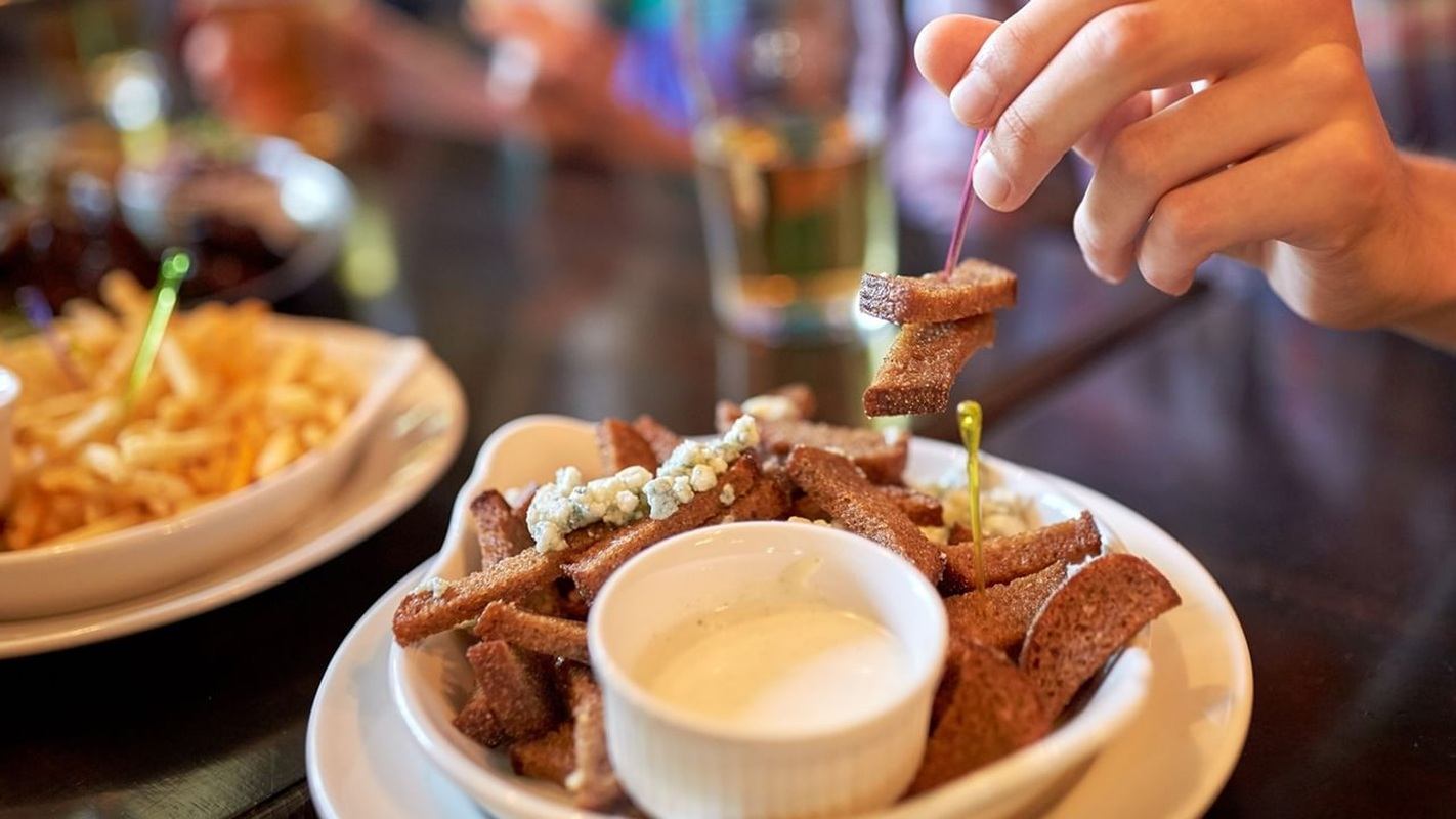 Plate of fried bread sticks with dip as hand lifts a piece.