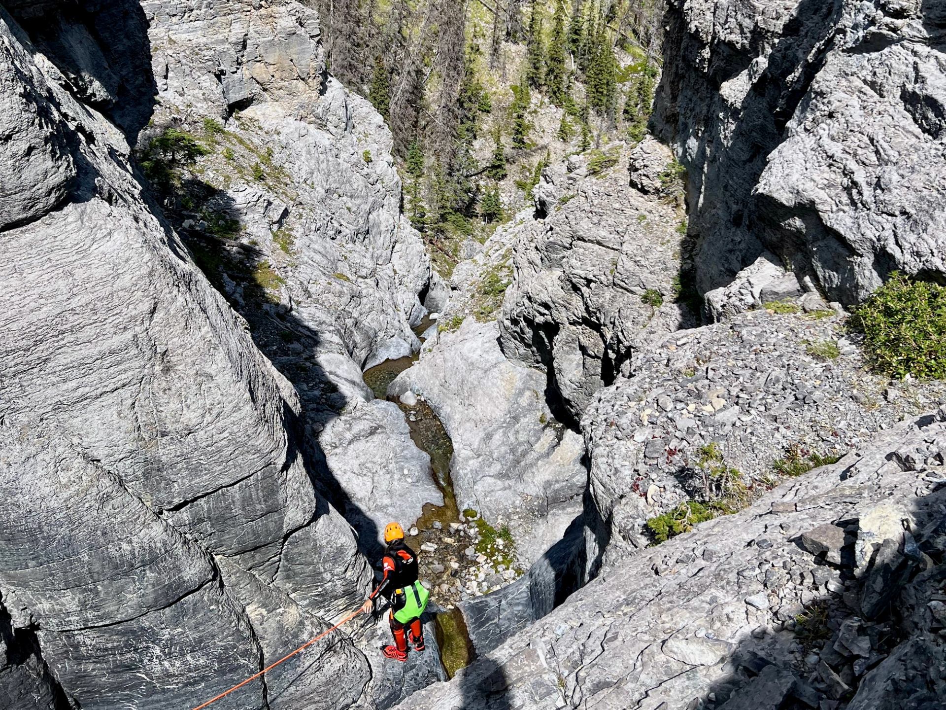 Person rappelling into a deep rocky canyon surrounded by rugged cliffs.