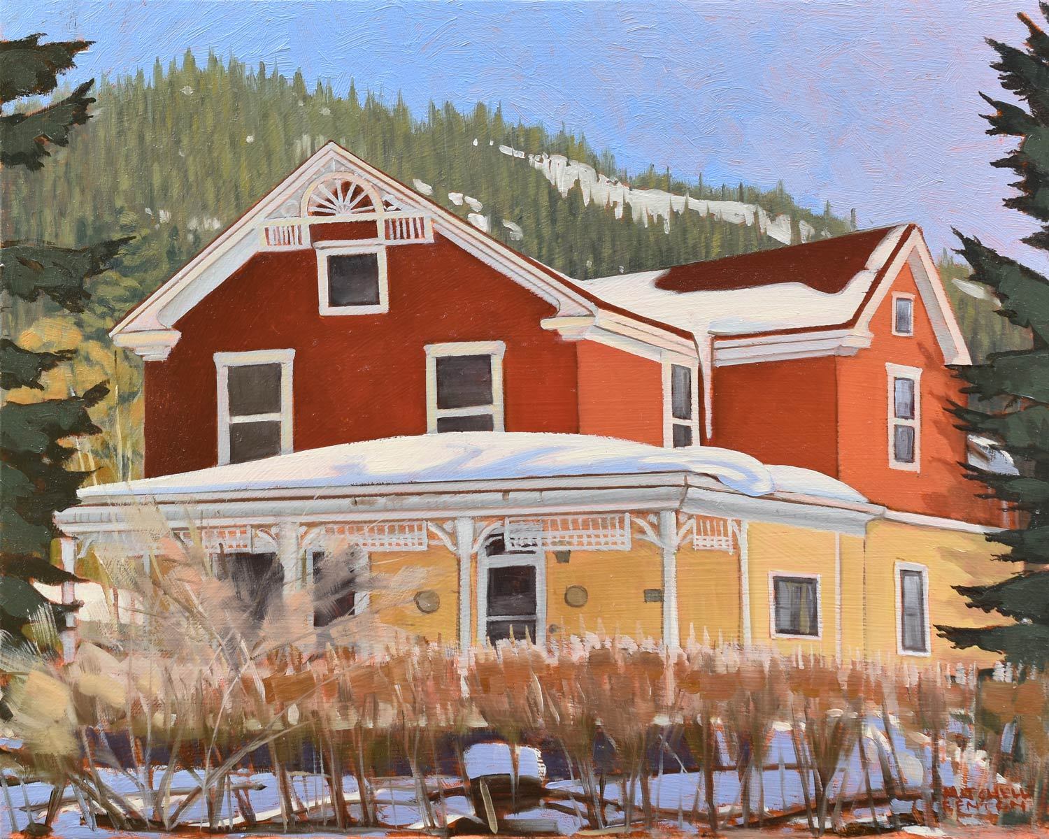 Red and yellow buildings under snow, with mountains and a forested hillside in the background.