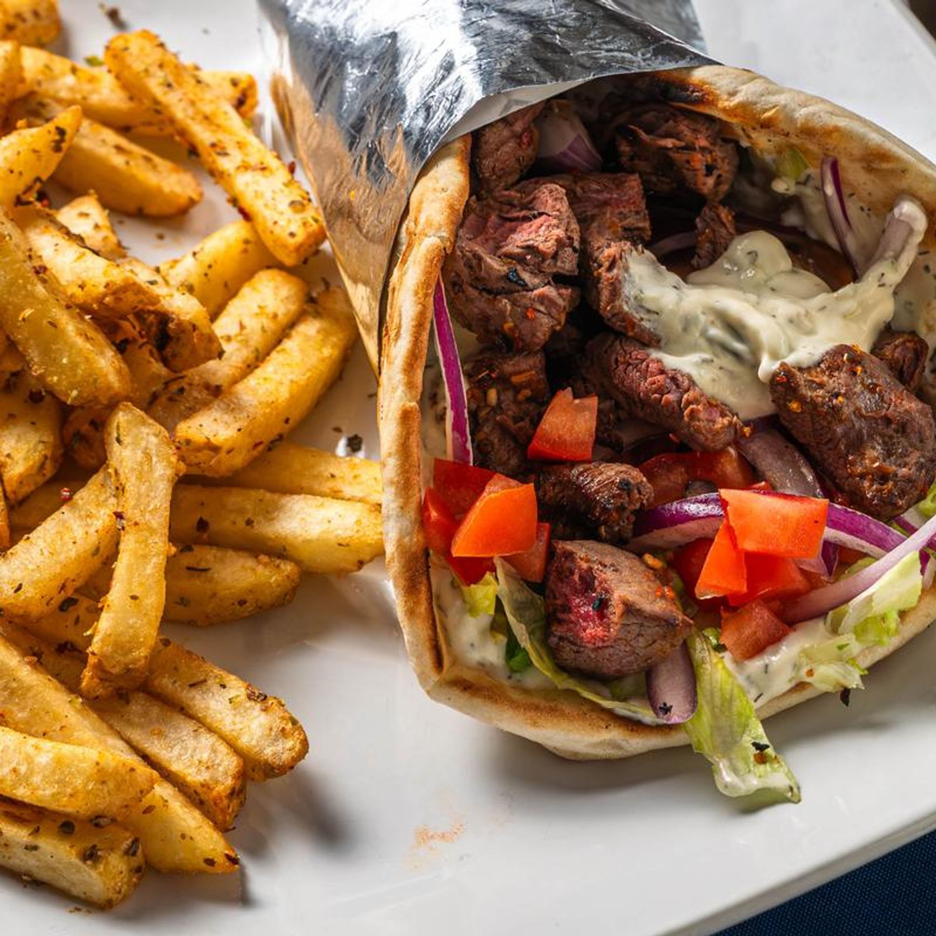 A Greek-style pita wrap filled with grilled meat, vegetables, and sauce is served with seasoned fries.