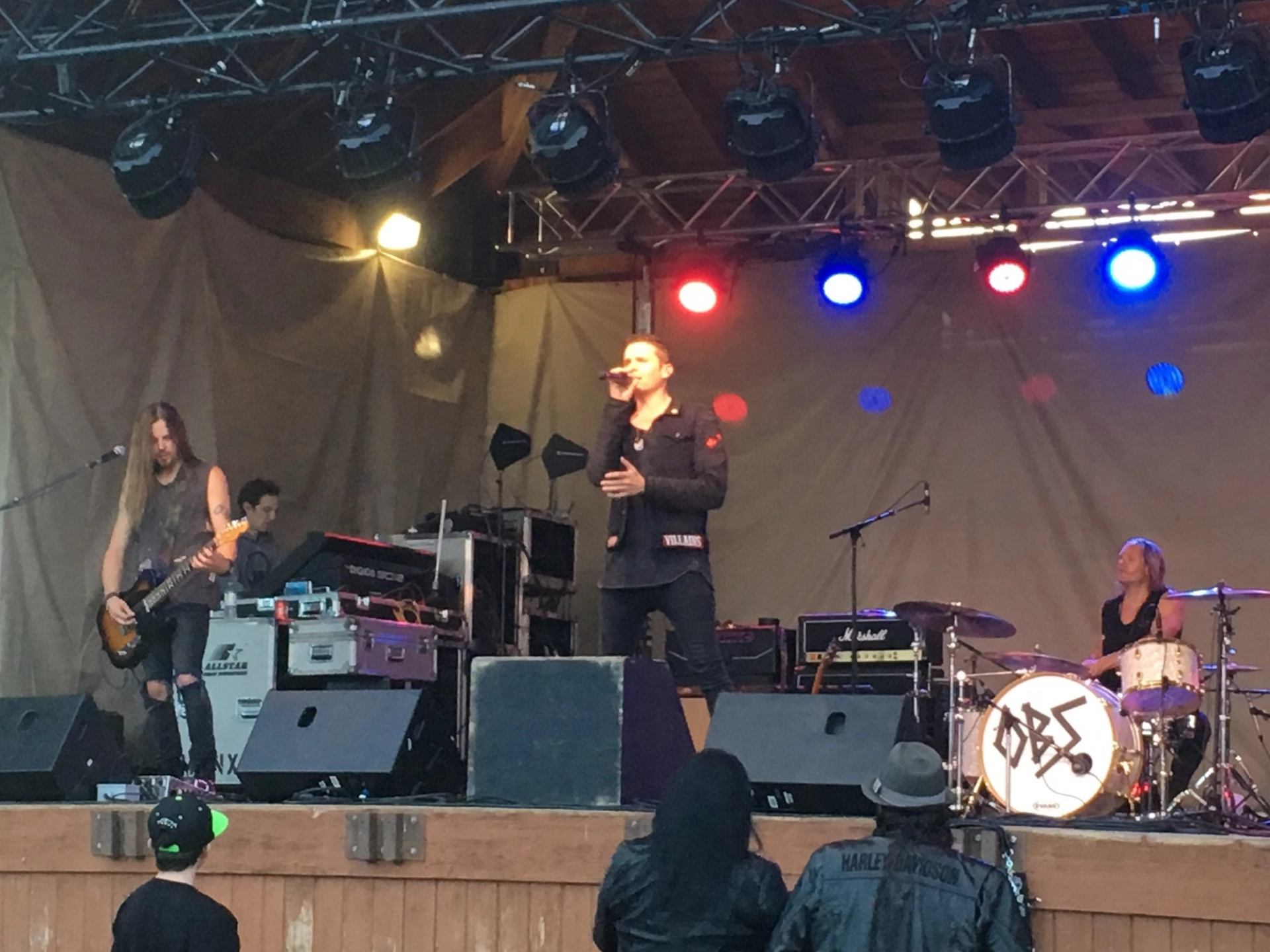 Rock band performs on outdoor stage with singer, guitarist, drummer and colourful stage lights.