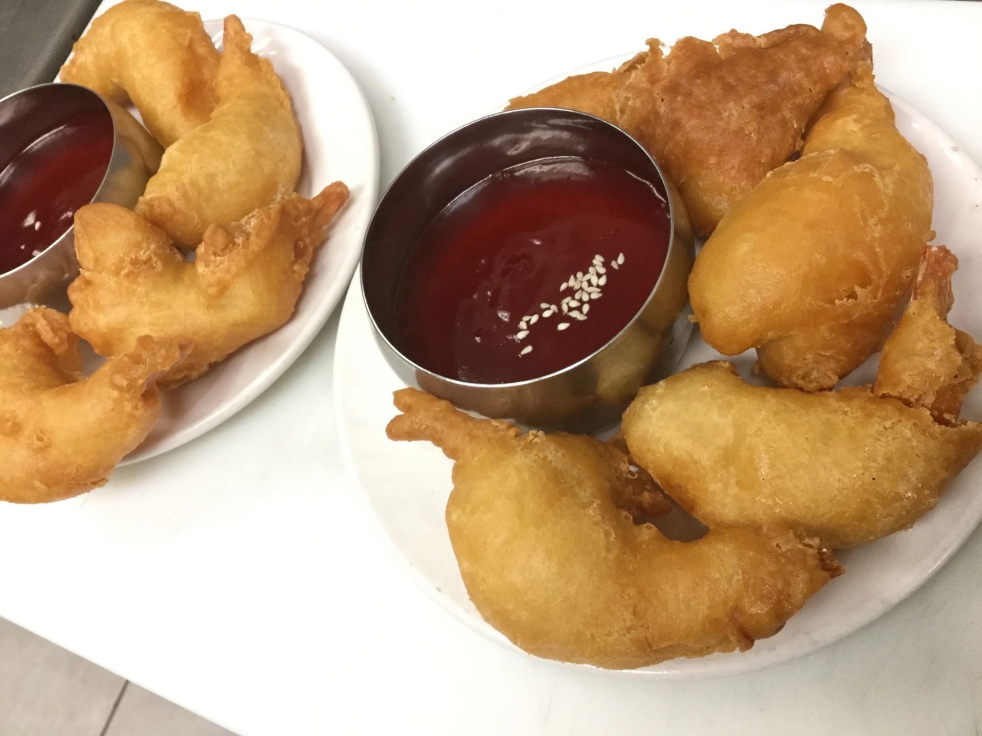 Two plates of fried food with red dipping sauce topped with sesame seeds.
