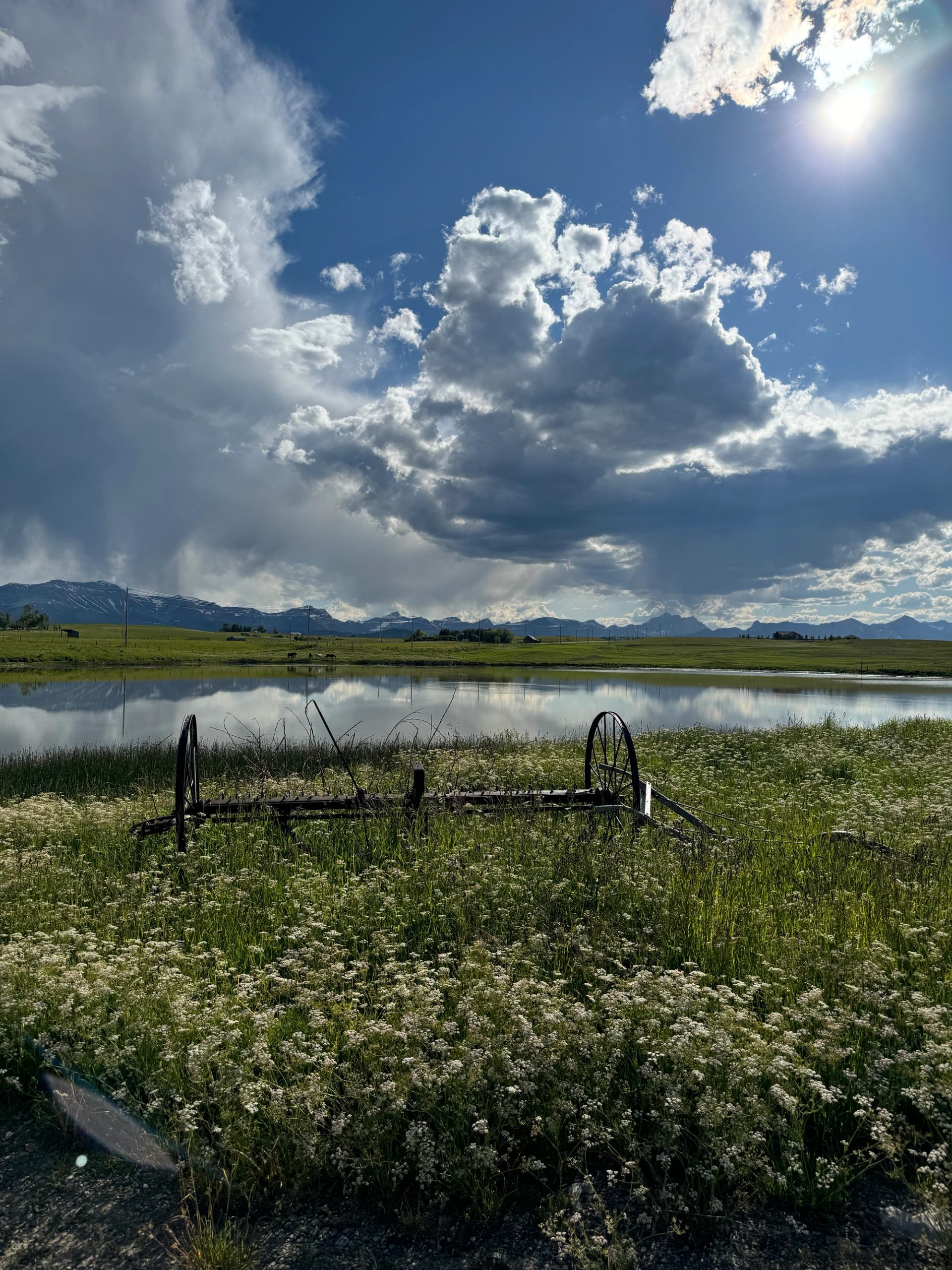 A calm lake surrounded by fields and mountains under dramatic cloud-filled skies.