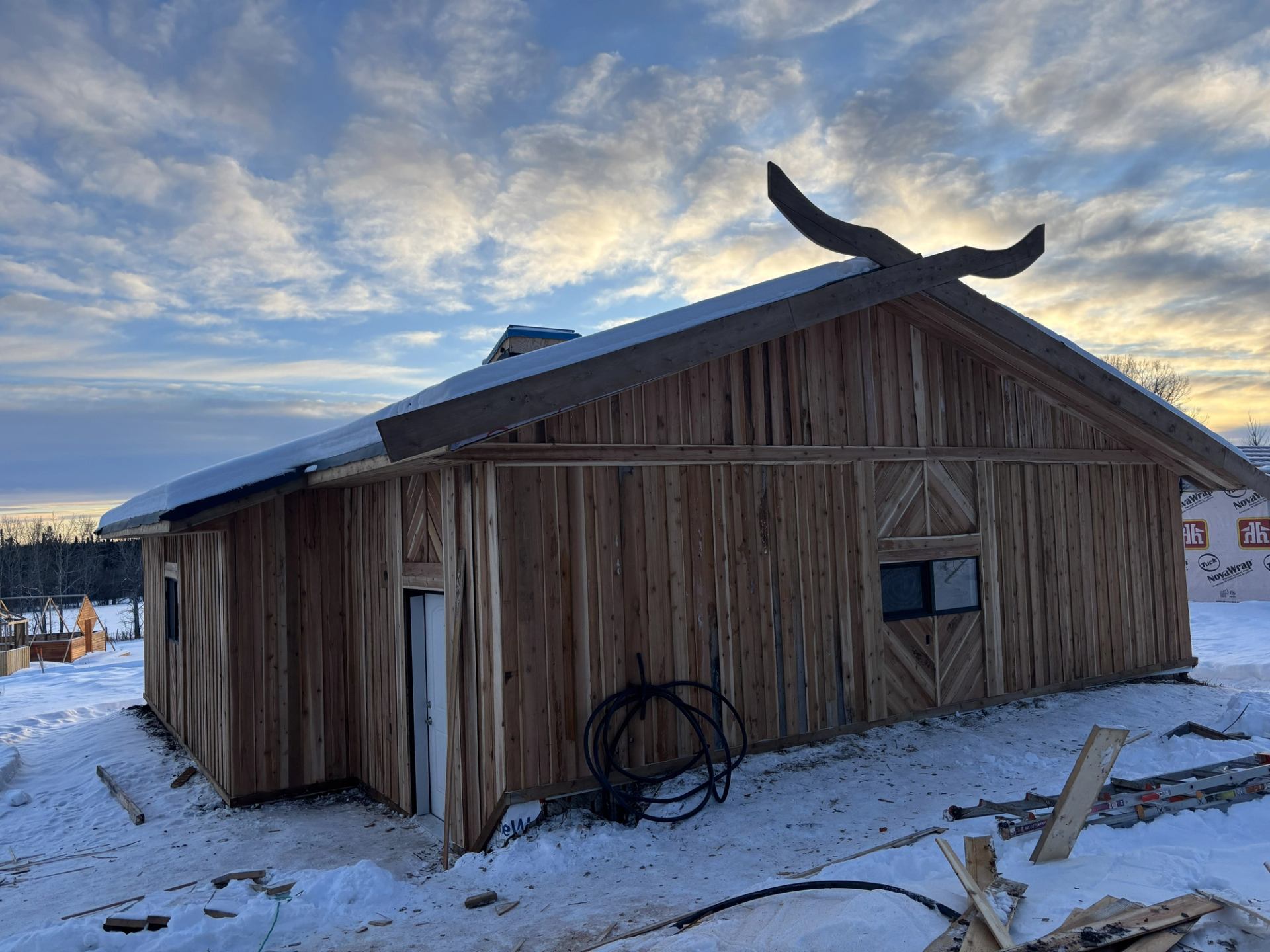Viking-style wooden building with horn-shaped roof finials in a snowy landscape.