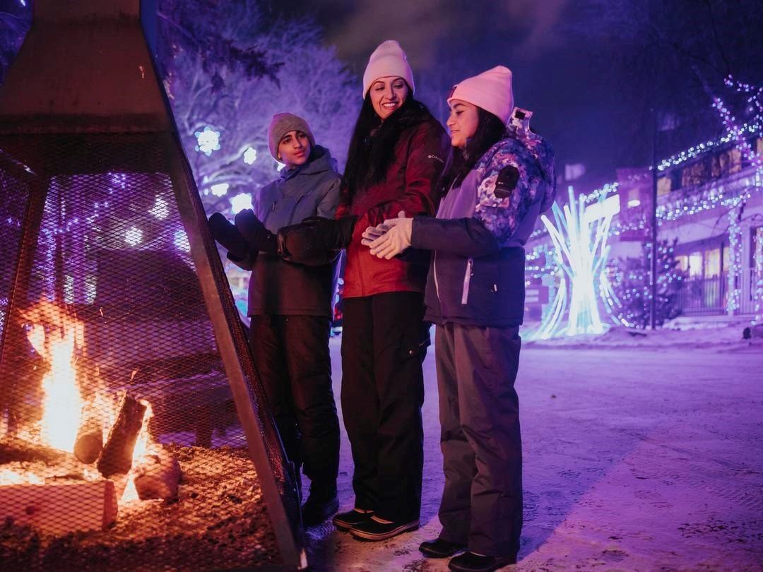 Three people warming hands by outdoor fire in snowy evening