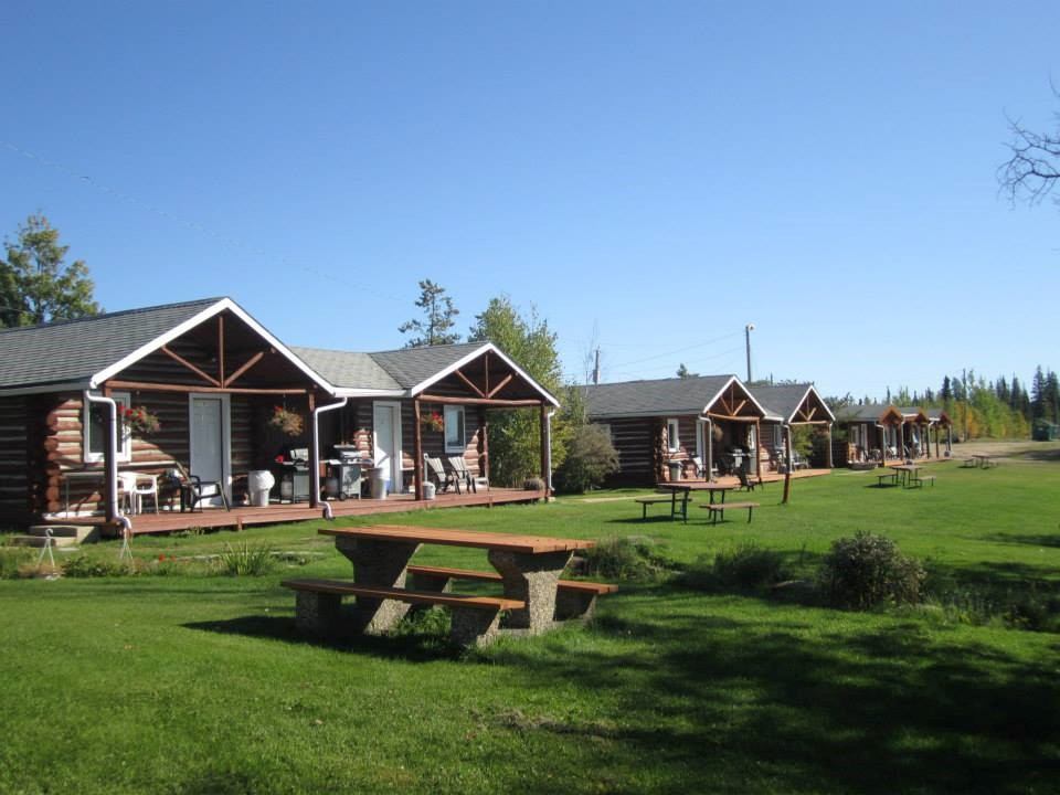 Row of log cabins with porches and a picnic table on a grassy lawn.