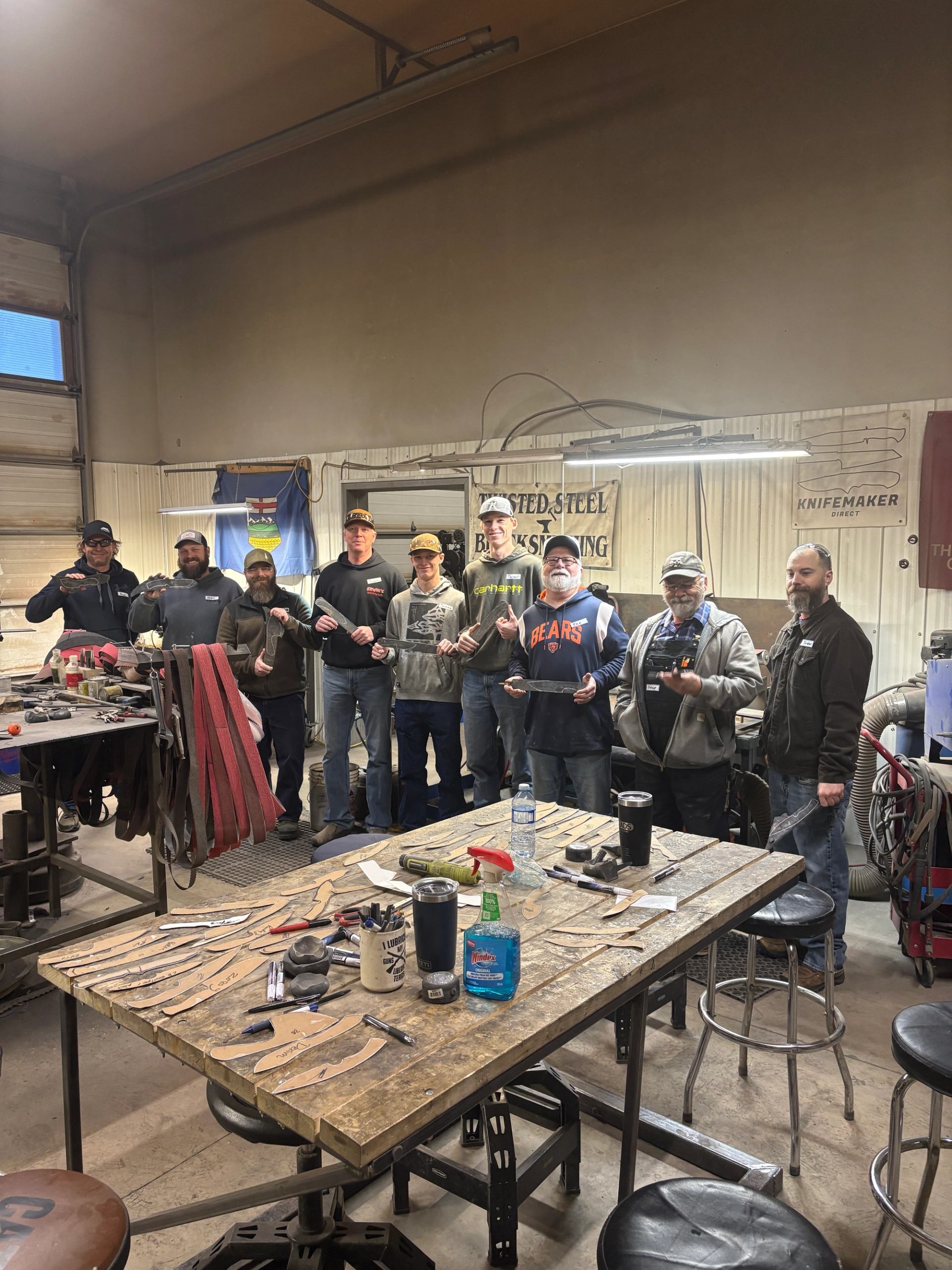 Group of students standing in a workshop holding the knives they made in class.