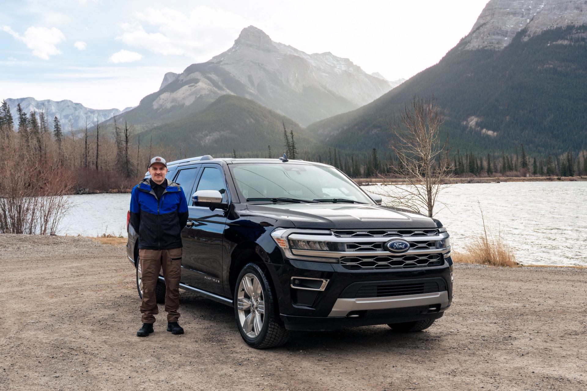 Guide standing beside a black SUV near Abraham Lake with mountains in the background.