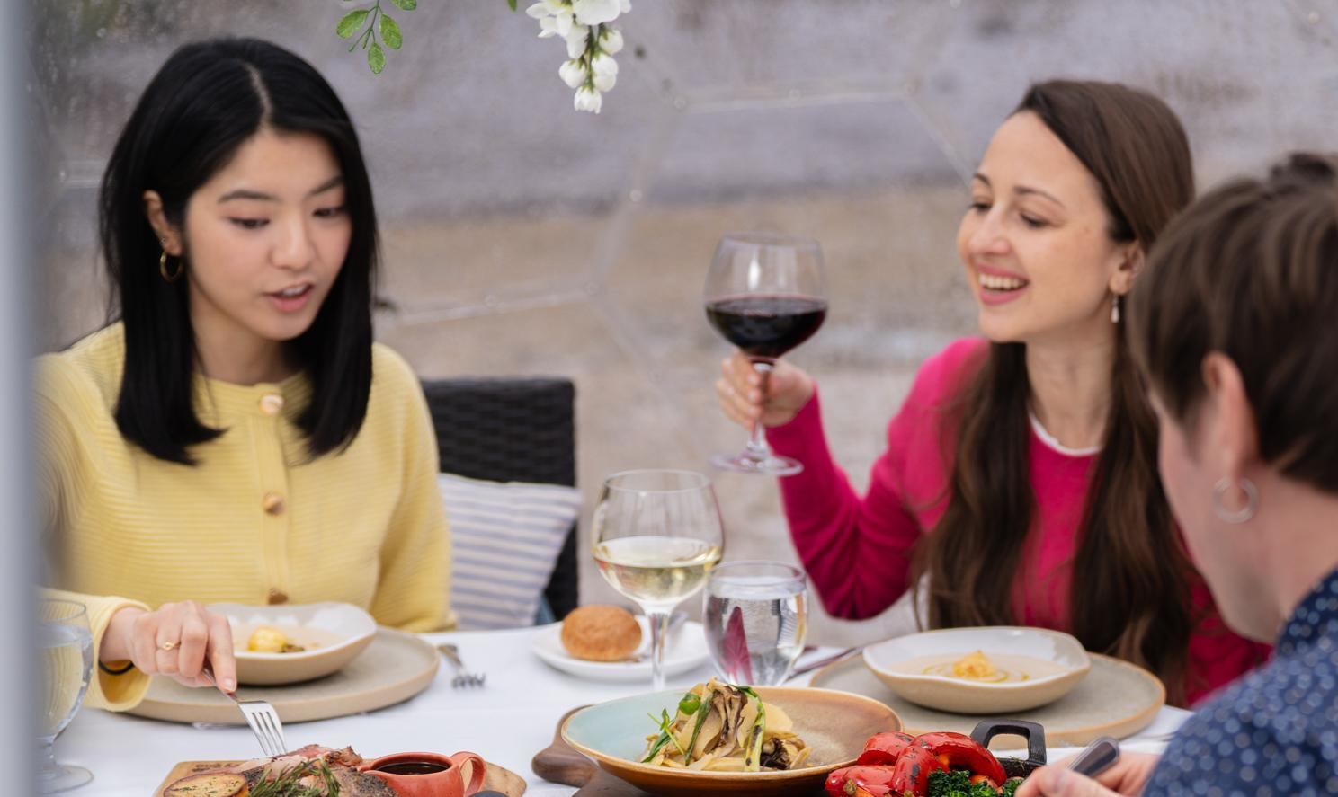 Guests dine and toast at a white table with plated brunch food and wine.
