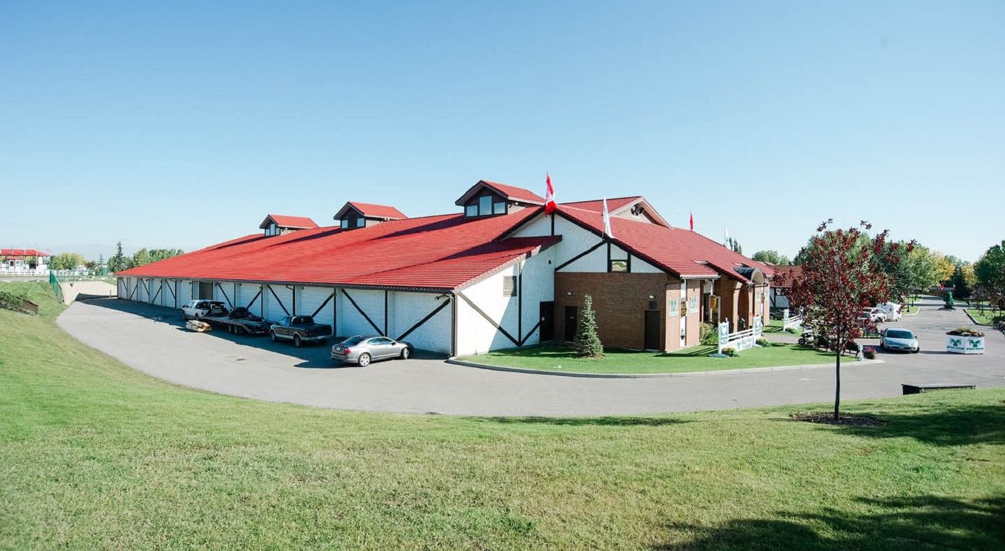 Building with red roof and white walls on a sunny day, surrounded by green grass and parking area.