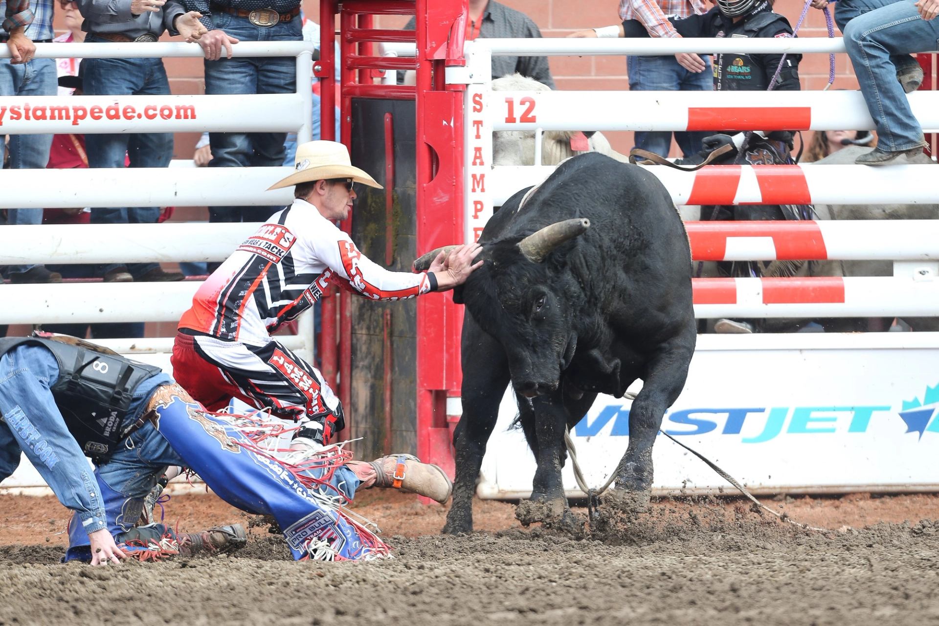 Bullfighter distracts charging bull as fallen rider scrambles away.