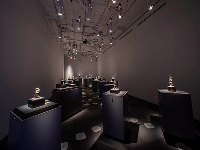 Gallery room with spotlit sculptures on black pedestals under ceiling track lights.
