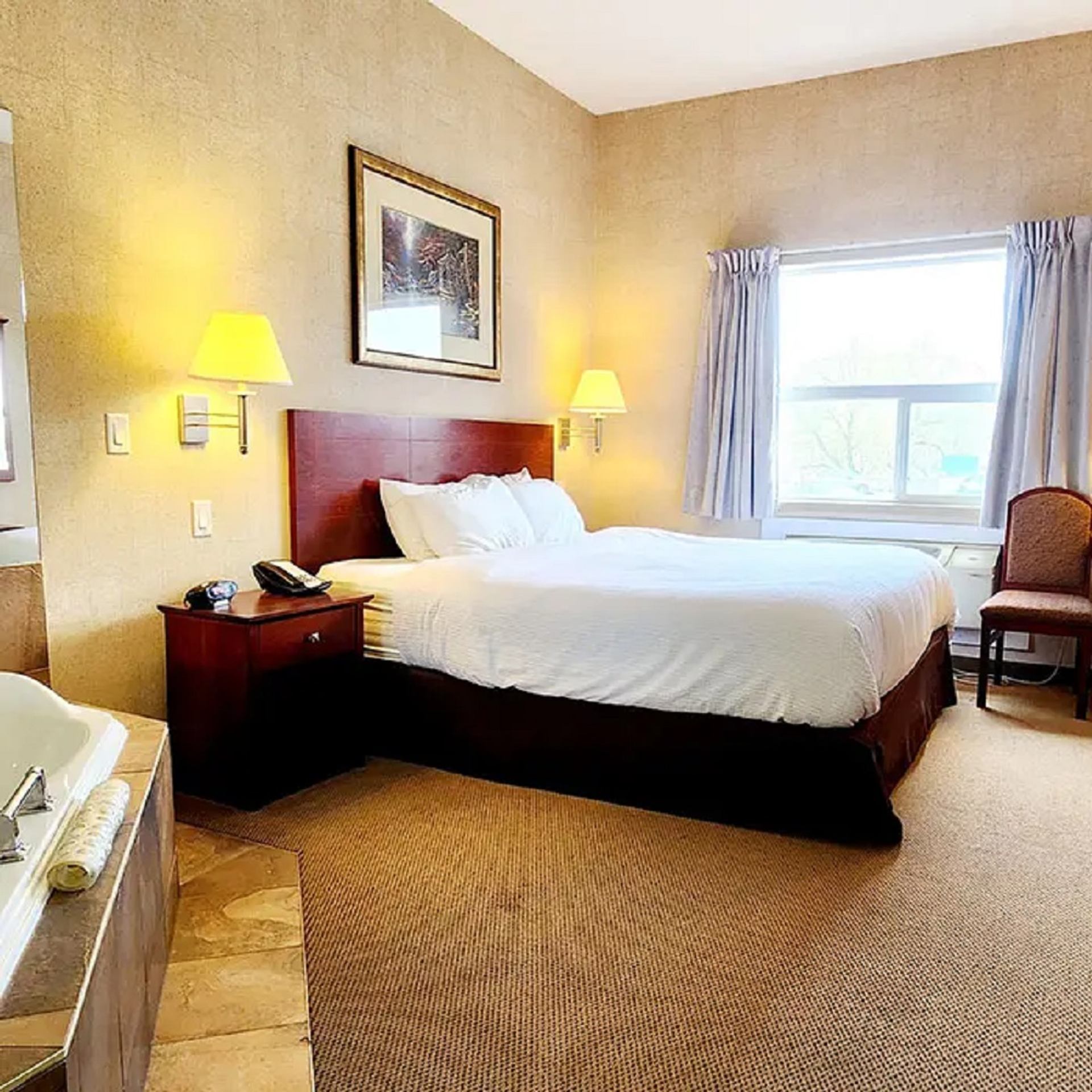 Bright hotel room with a queen bed, warm lighting, and a window view at Park Hill Inn & Suite.