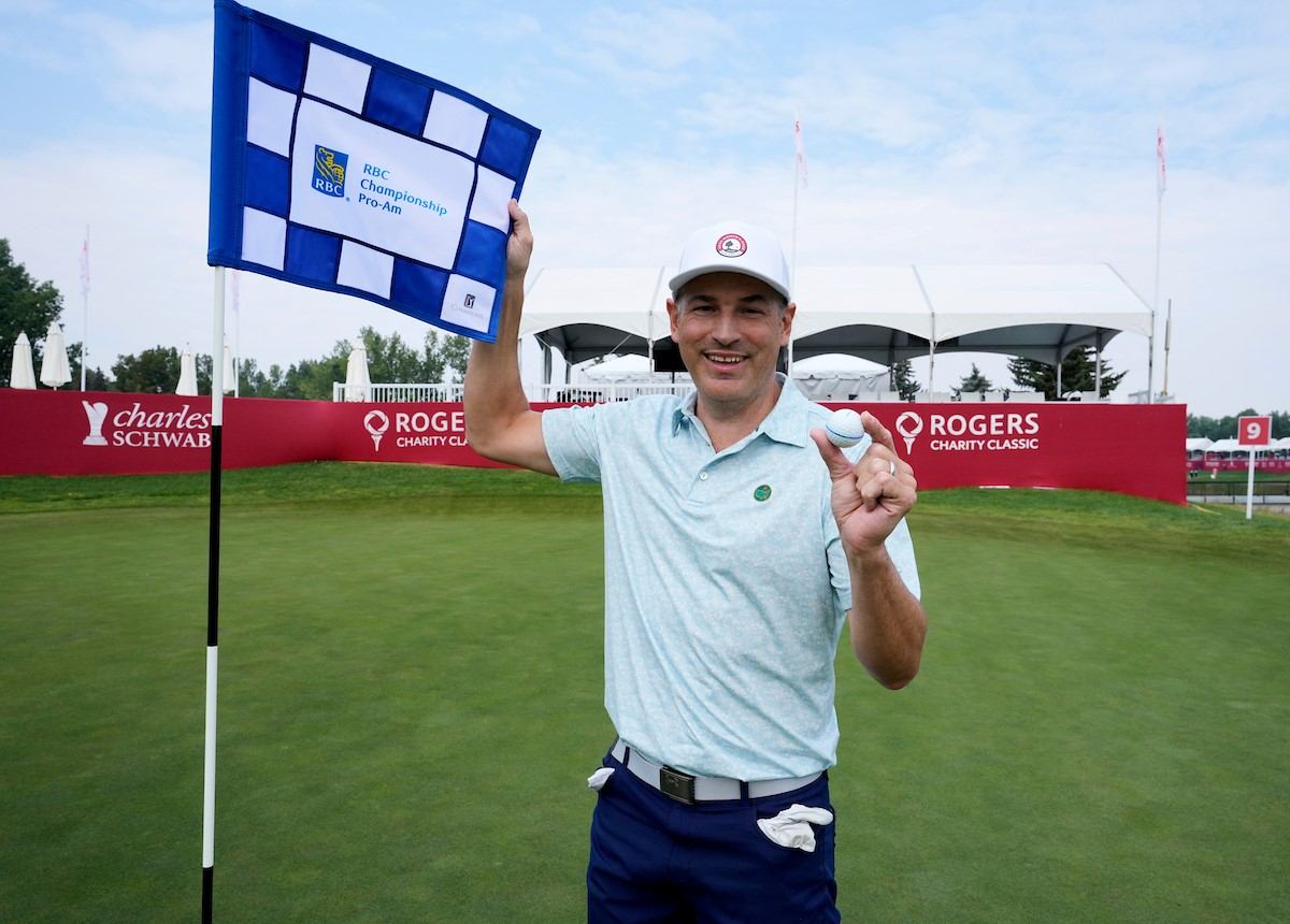 Golfer holding RBC Championship Cup and waving at Rogers Charity Classic banner at Calgary venue.