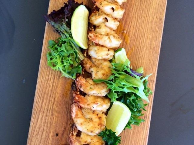 Grilled shrimp arranged on a wooden board with greens and lime wedges, ready to serve.