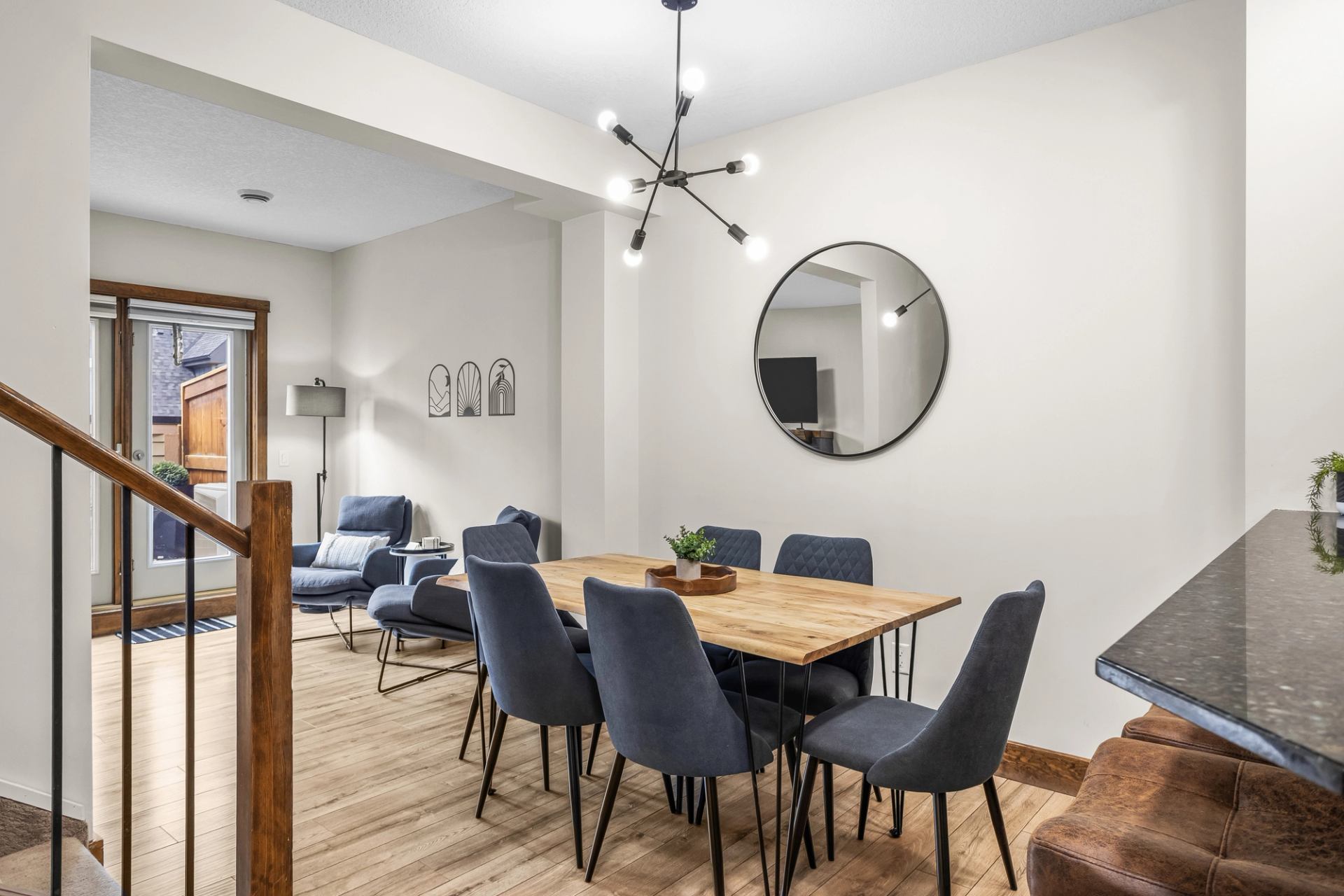 Dining area with wooden table, dark chairs, round mirror and modern chandelier.