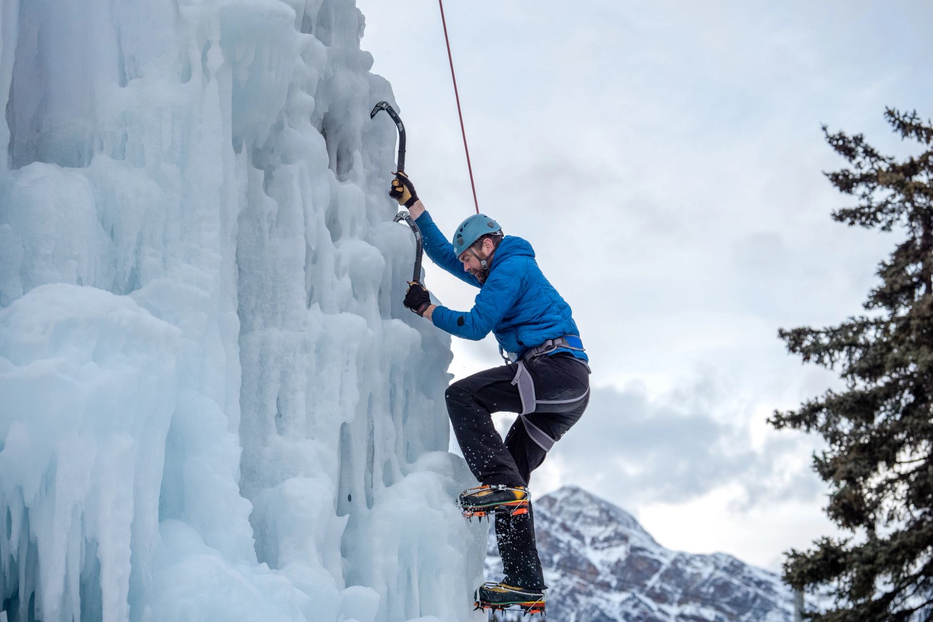 Ice climber scaling a vertical ice wall in snowy Jasper mountain terrain.