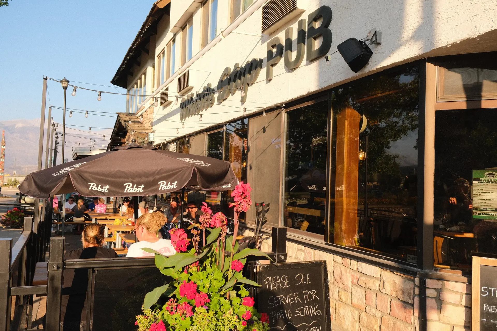 Pub exterior with outdoor seating, umbrellas, and pink flowers in daylight.