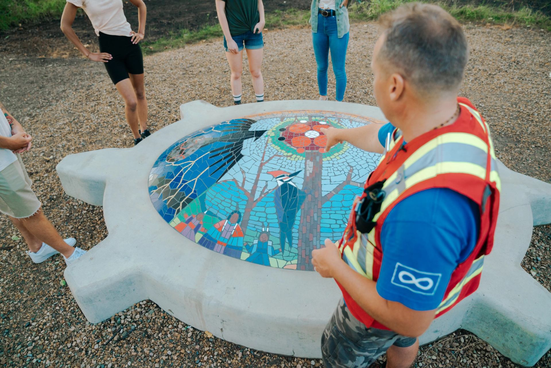 Group gathers around artwork of a mosaic turtle with birds and nature designs depicted.