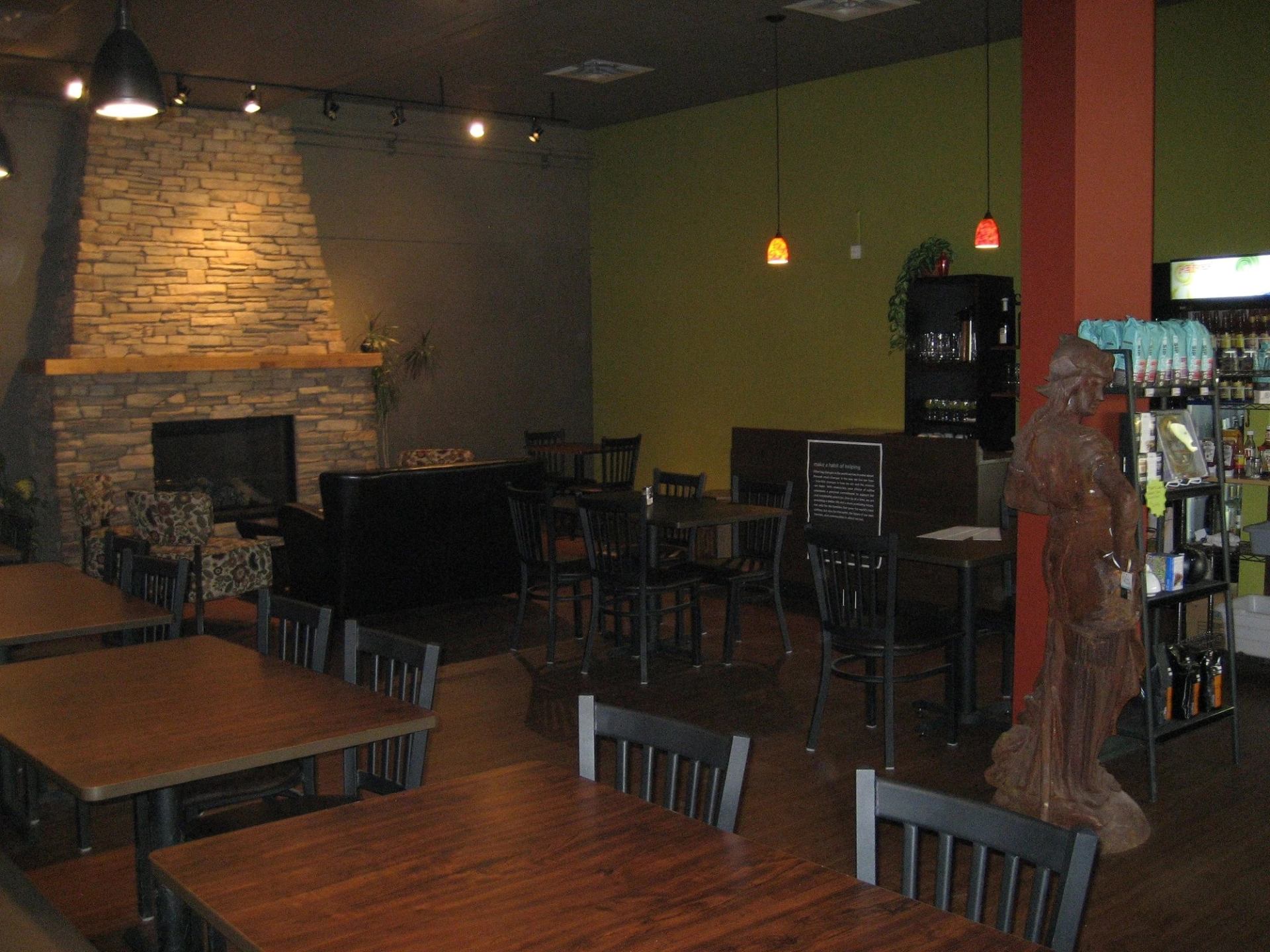 Restaurant dining area with wooden tables, stone fireplace, pendant lights and carved statue.