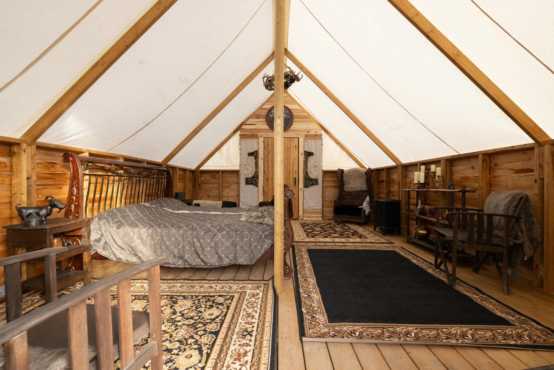 Interior of a glamping tent with a bed, seating area, wooden walls, and canvas ceiling.