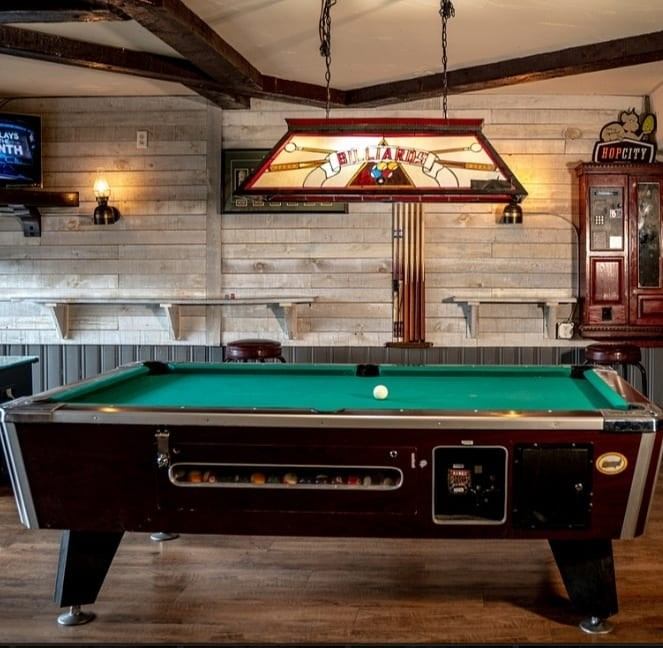 Rustic pool table setup with stained glass light in cozy bar room.