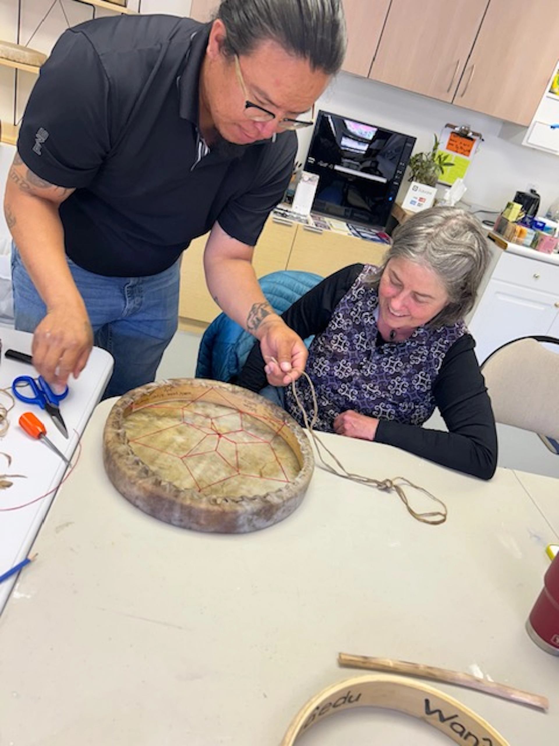 Two people crafting a drum with tools and circular frames.