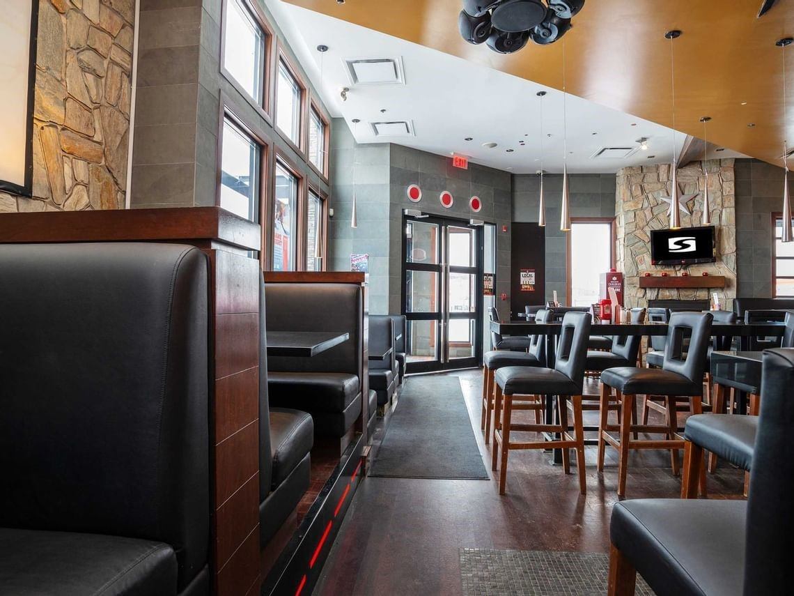 Restaurant lounge interior with leather booths, high-top tables, stone walls and tall windows.